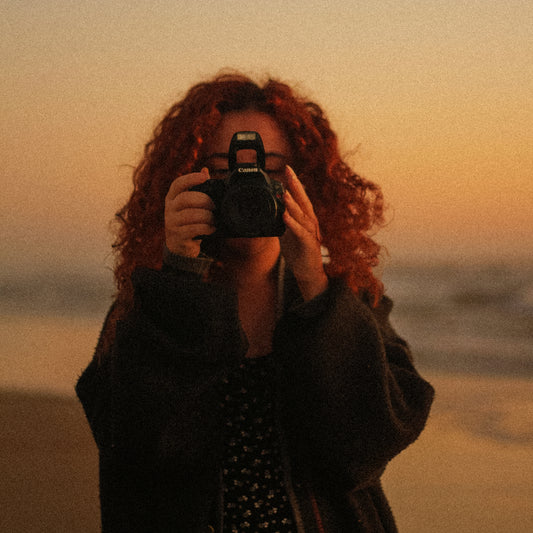 Person with curly hair holding a camera against a sunset sky - Agfa Precisa film emulation preset by PresetVault
